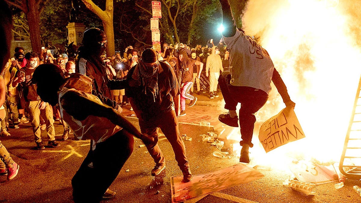 Protesters climb street sign near burning barricade during unrest in Washington.