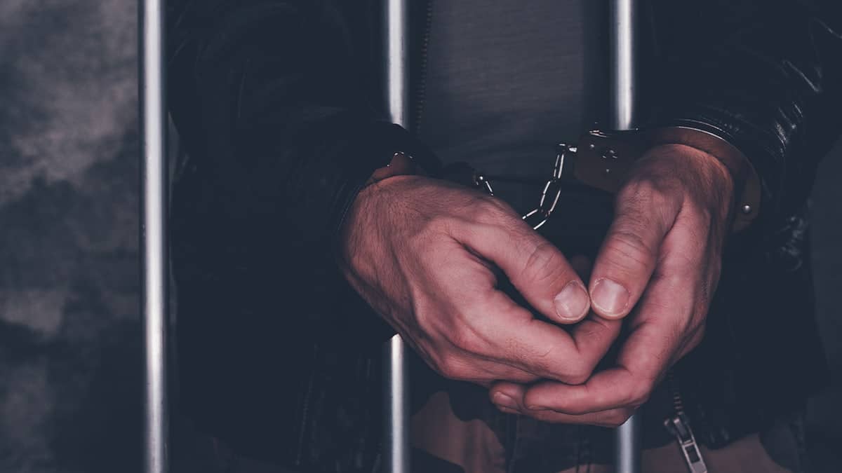 Handcuffed man standing behind prison bars