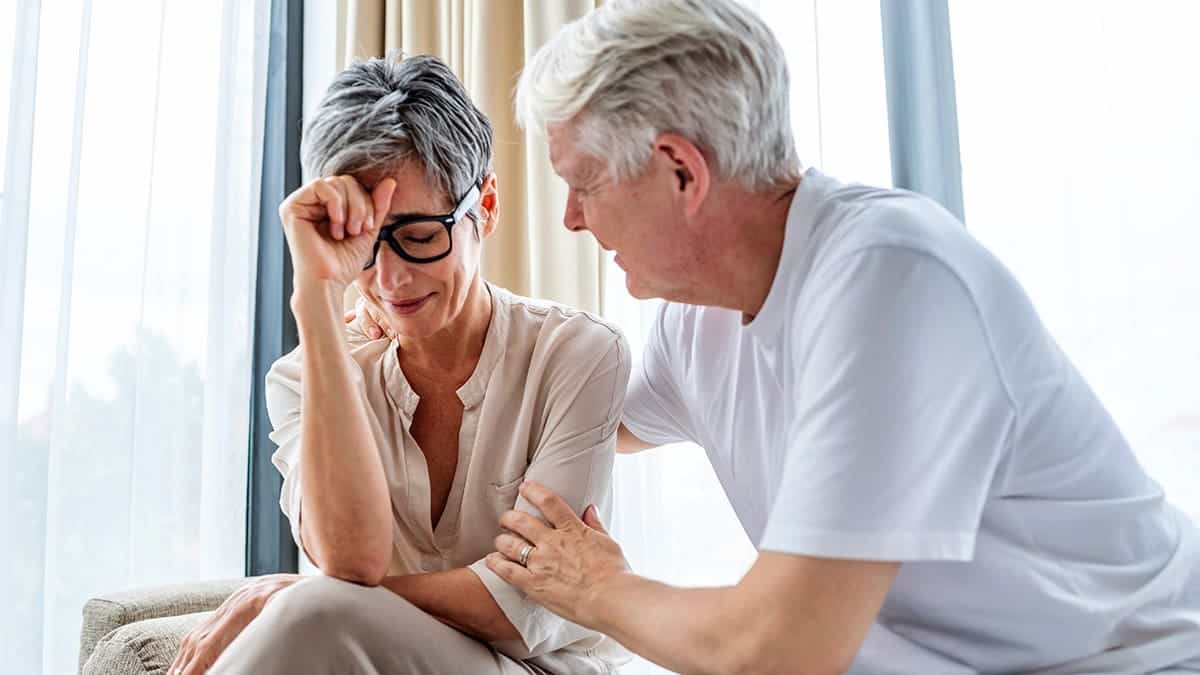 A husband comforting his distressed wife seated in a bright cozy room