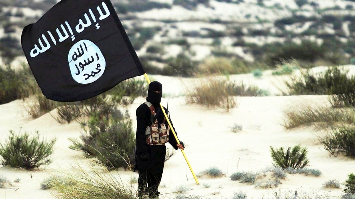 Masked Islamic State fighter holding ISIS flag in desert