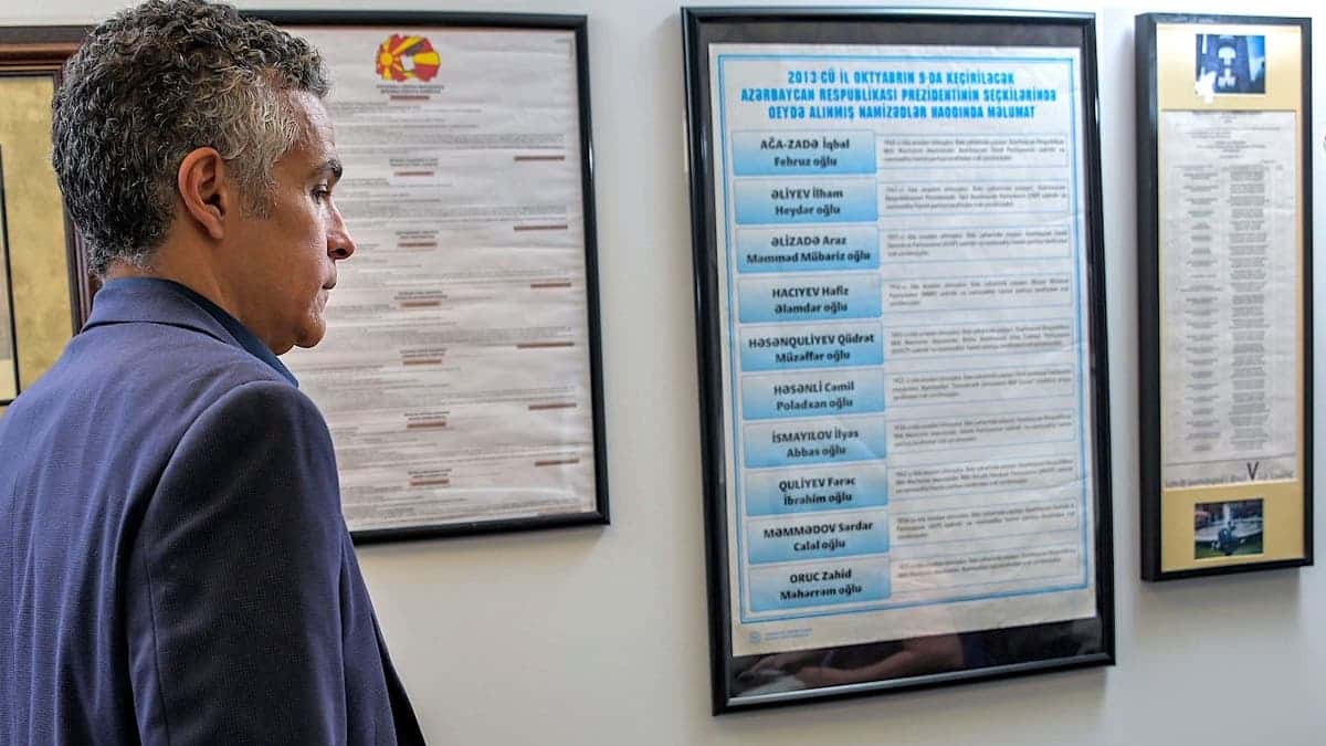 Jared DeMarinis standing in an office with sample ballots from North Macedonia, Azerbaijan and Armenia hanging on the wall