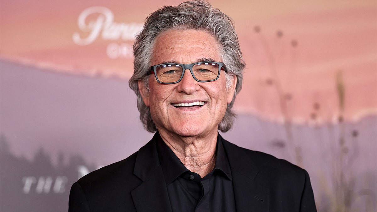 Kurt Russell standing on a red carpet at an event.
