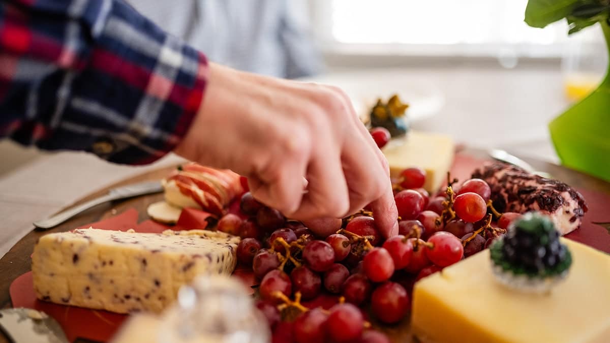 Man's hand picking grapes from a cheese and fruit platter.