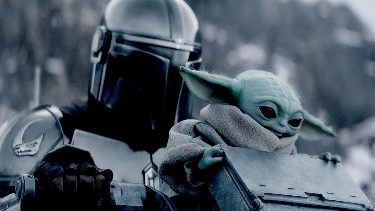 Pedro Pascal as The Mandalorian holding Grogu in a scene from The Mandalorian.