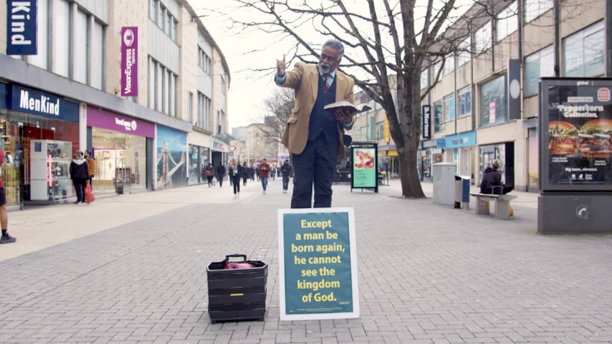 Pastor Dia Moodley preaching on a street corner in Bristol holding a Bible