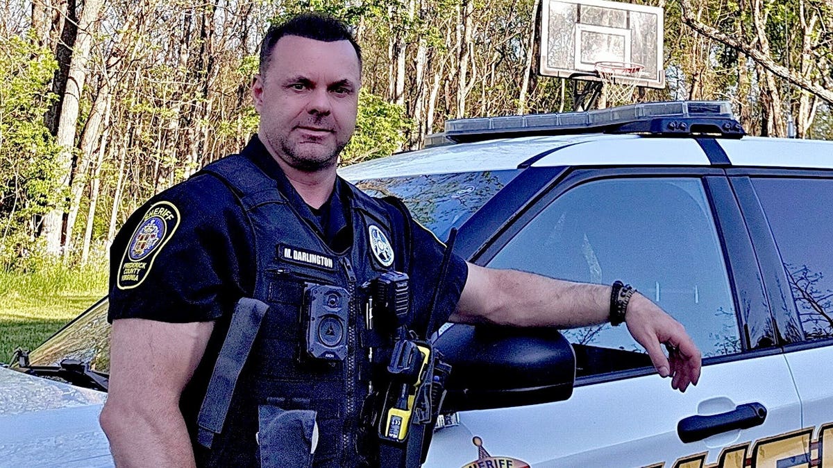 Frederick County Deputy Sheriff Chris Darlington poses next to his police car.