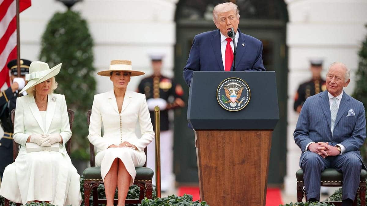 President Trump giving a speech with Melania Trump, Queen Camilla and King Charles sitting behind him.
