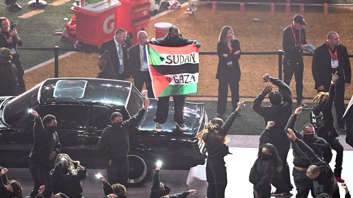 Protestor holding Palestinian flag with Gaza and Sudan text during Kendrick Lamar performance