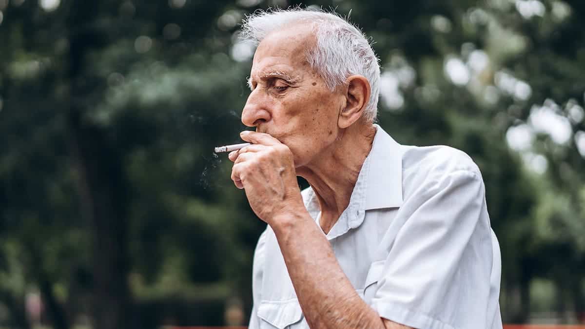 Senior adult men smoking cigarettes while sitting on a park bench outdoors