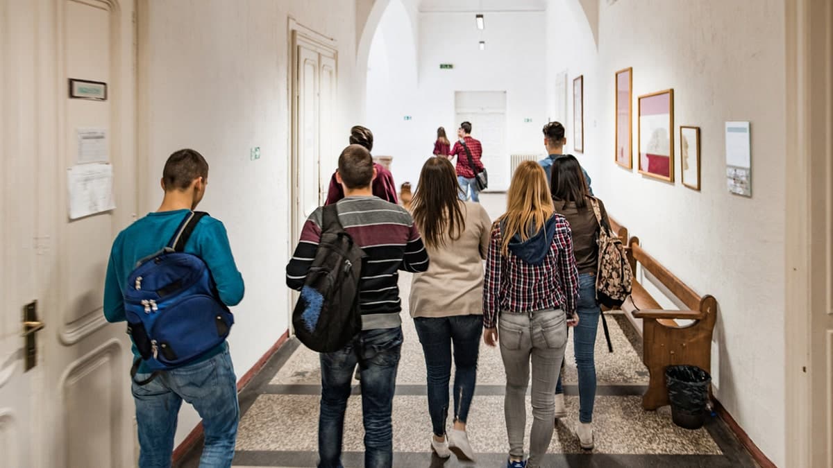 Rear view of high school students walking in a school hallway.