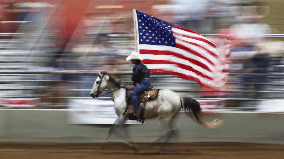 A cowboy on a horse waving an American flag in a rodeo arena.