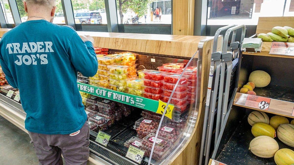 A Trader Joe's employee stocks a shelf of fruit inside a store.