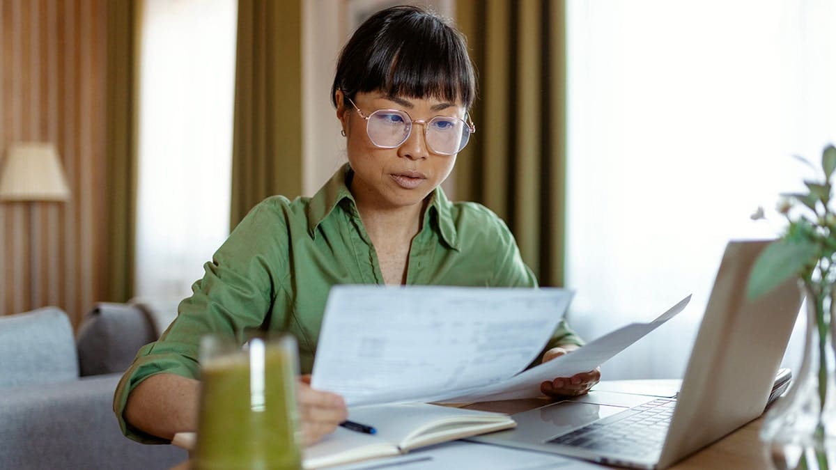 A woman looks at forms in front of a laptop.