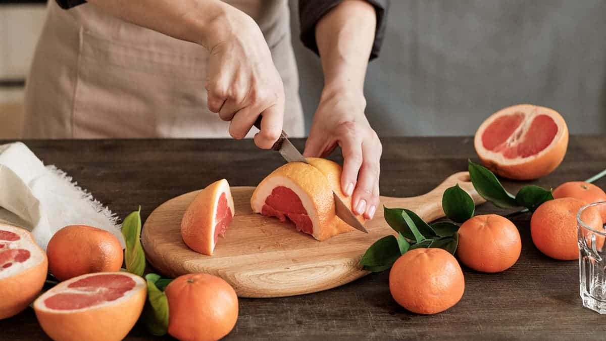 A woman cuts a grapefruit on a cutting board.