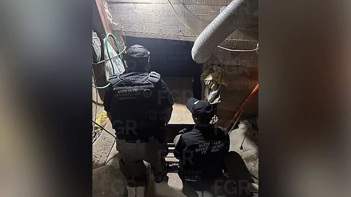 Two Mexican federal investigators stand beside an opening leading into an underground tunnel inside a building.
