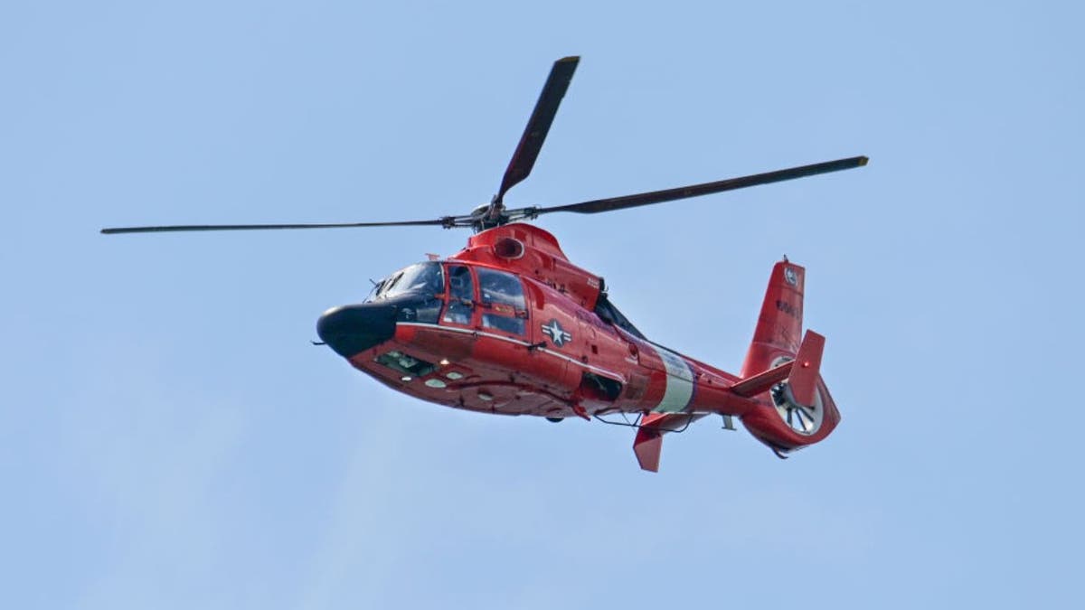 A U.S. Coast Guard Search and Rescue helicopter flying over a river area.