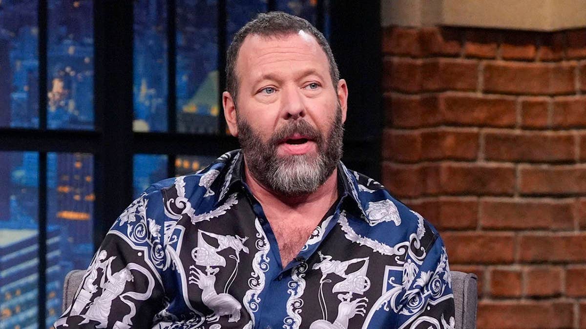 Comedian Bert Kreischer sitting and talking with host Seth Meyers on a late night show set