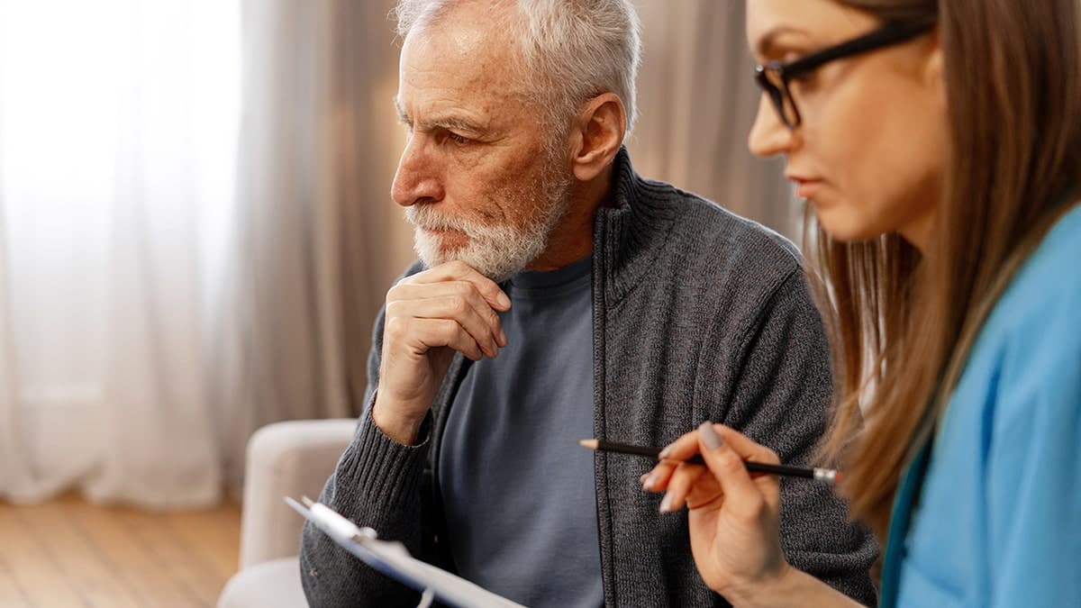 Man discussing medical history with doctor during home visit as doctor takes notes