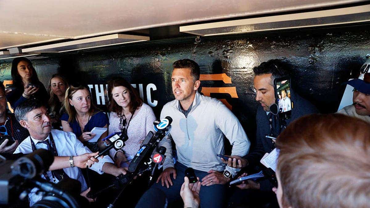 Buster Posey speaking at a microphone at Oracle Park in San Francisco