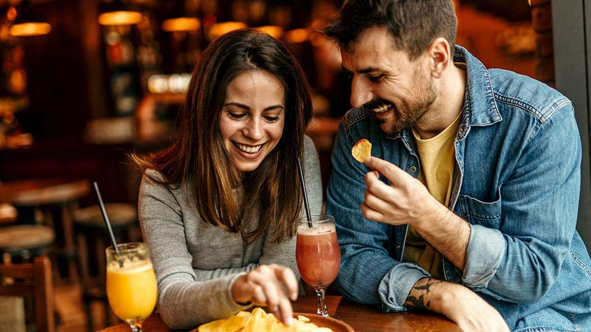 A couple drinks cocktails and snacks on potato chips.