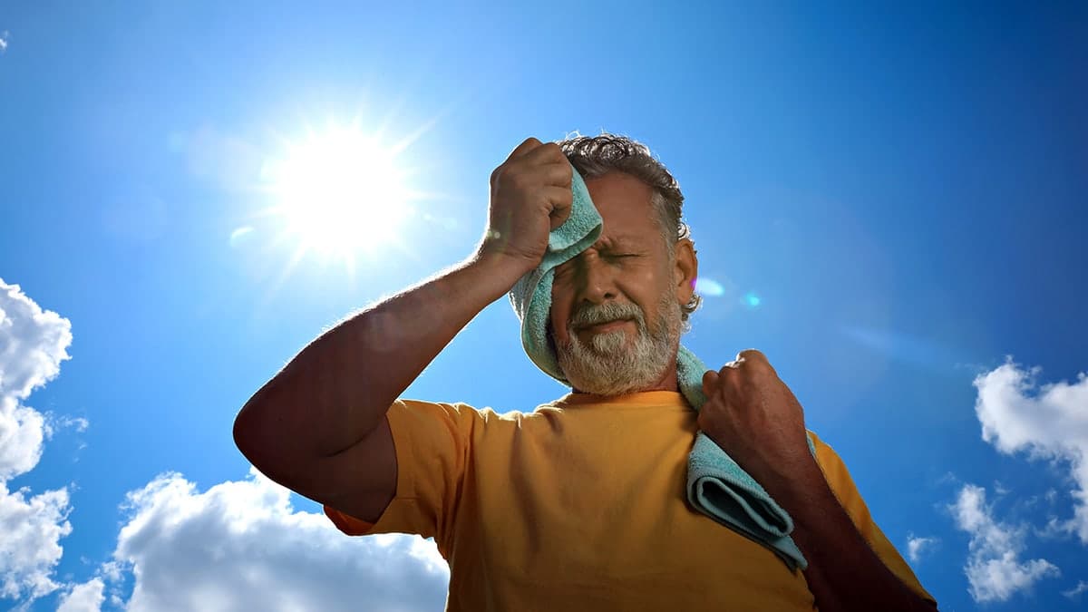 Senior man holding towel to his face outdoors appearing to suffer from heat stroke