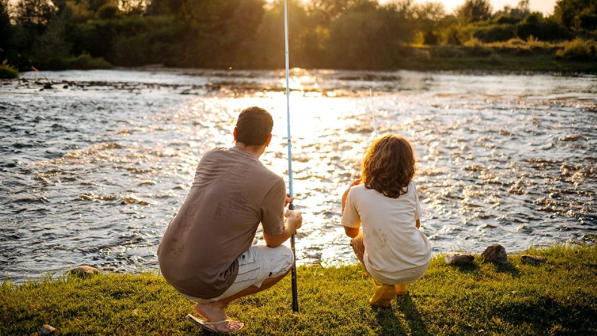 Father and child go fishing by shoreline.