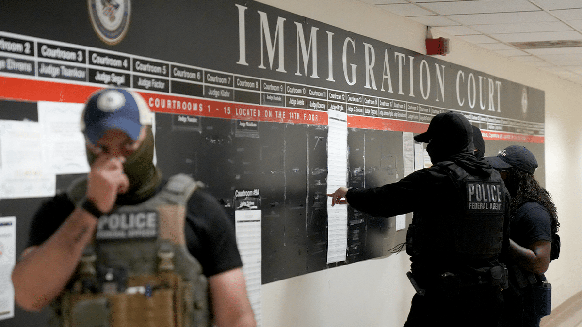 ICE agents reviewing lists of names and hearing times inside a courthouse hallway.