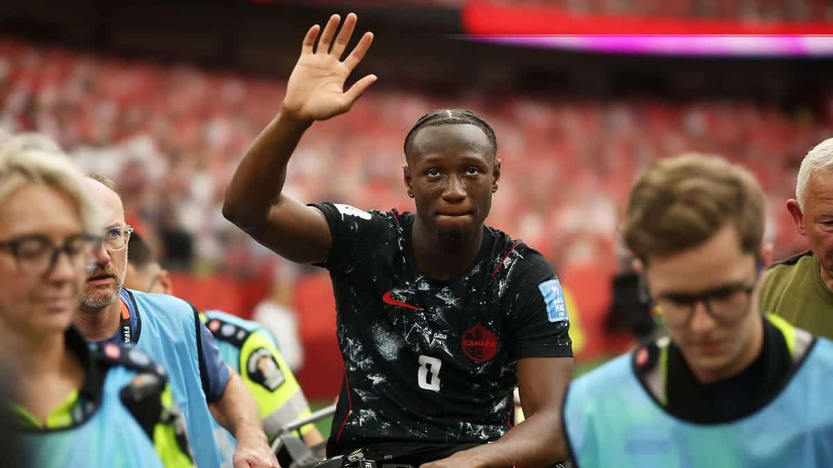 Ismael Kone of Canada waving to crowd while being stretched off soccer field.