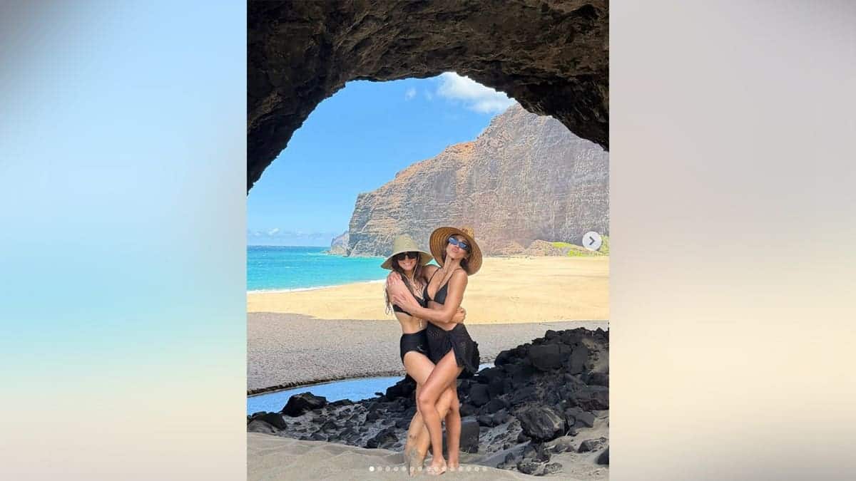 Jessica Alba and her friend at the beach standing under an arch.