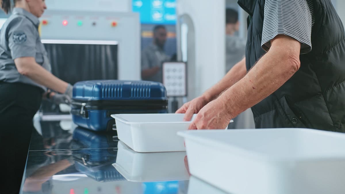 A traveler placing personal items in a tray at an airport security checkpoint with TSA officers screening luggage