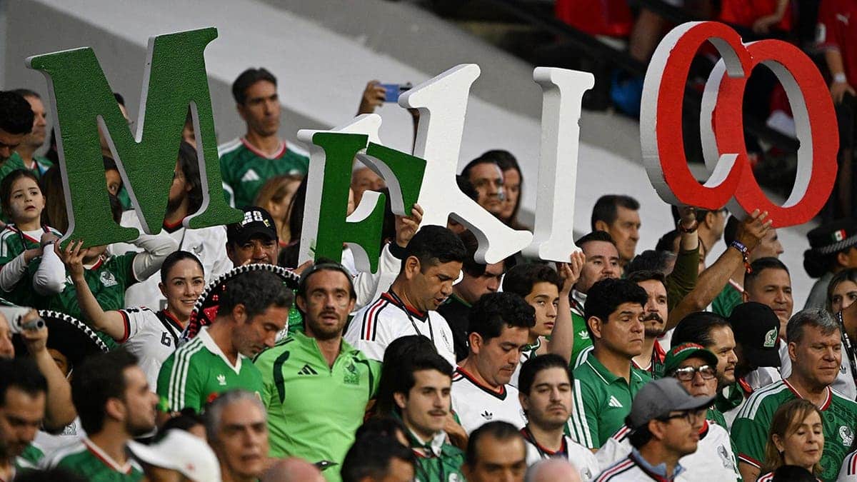 Mexican fans holding letters that spell Mexico cheering at a football stadium.