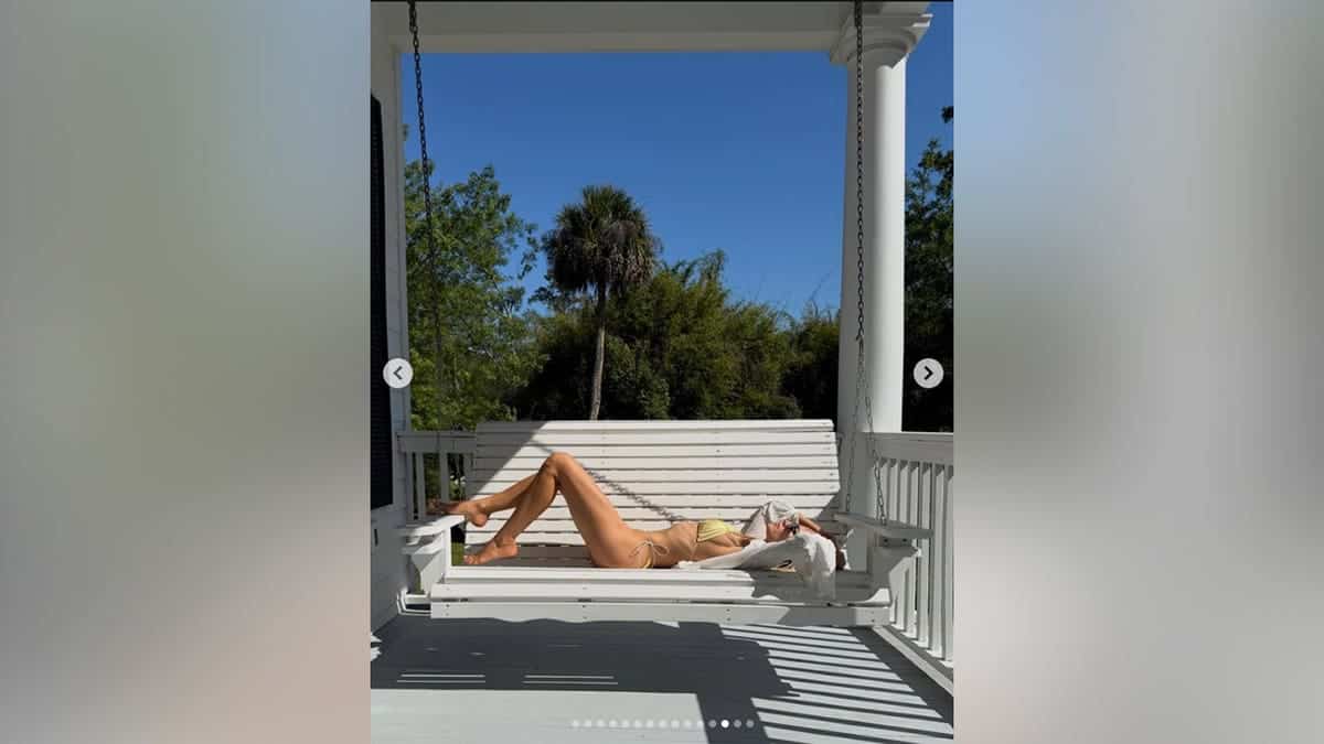 Michelle Randolph in a metallic yellow bikini on a porch swing in June 2026.