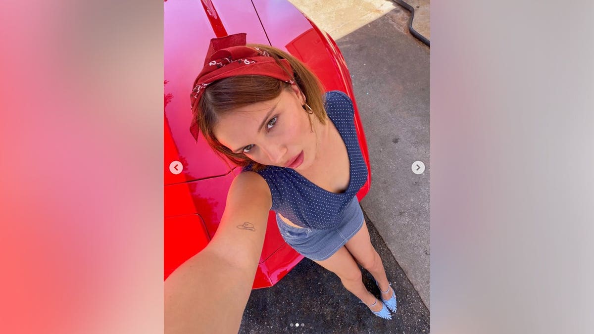 Millie Bobby Brown taking a selfie in front of a red convertible for Americana