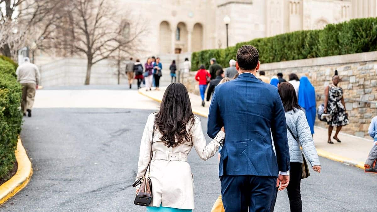 A couple holding hands walking on a street near the National Shrine of the Immaculate Conception in Washington, D.C.
