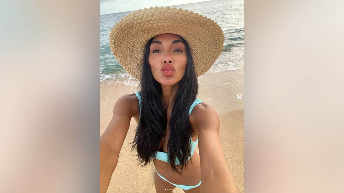 Nicole Scherzinger pursing her lips at the camera as she poses in a bikini on the beach.