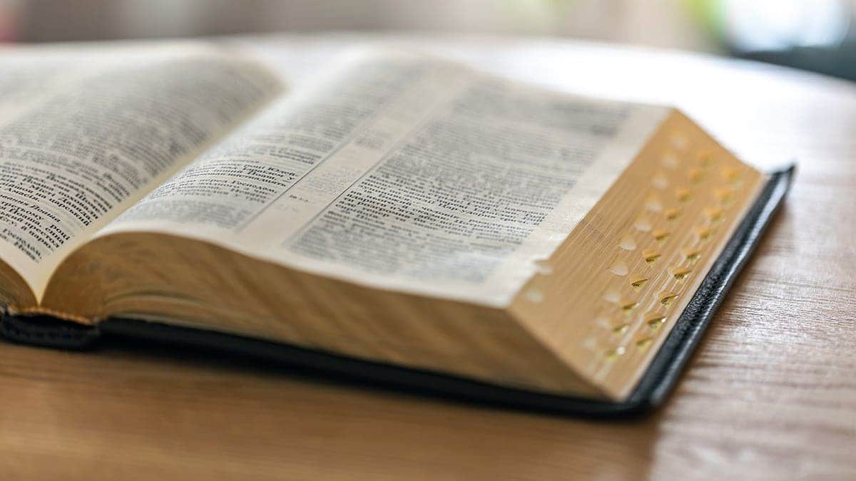 An open Bible resting on a wooden surface with visible text and golden edges.