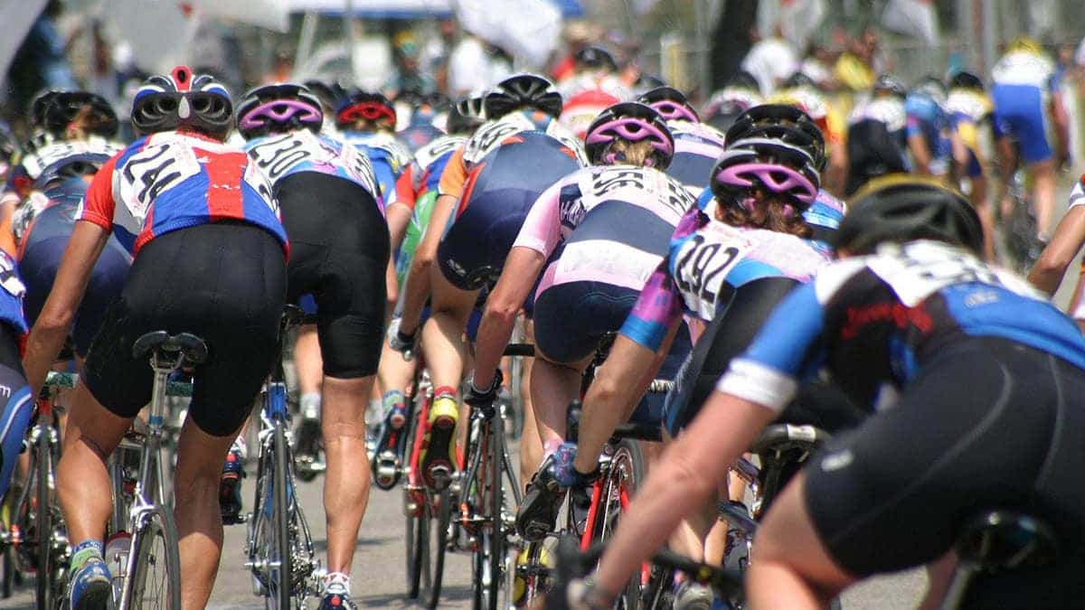 A peloton of cyclists riding closely together on a road.