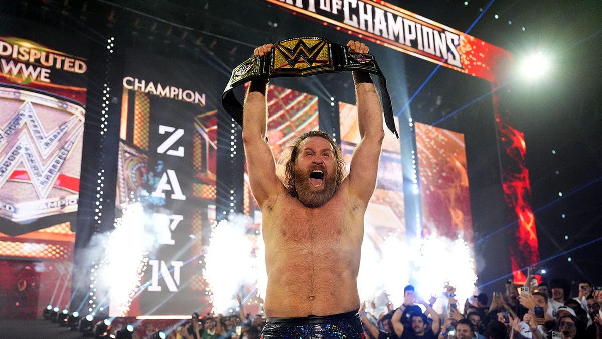 Sami Zayn holding the Undisputed WWE Championship belt in a wrestling arena.
