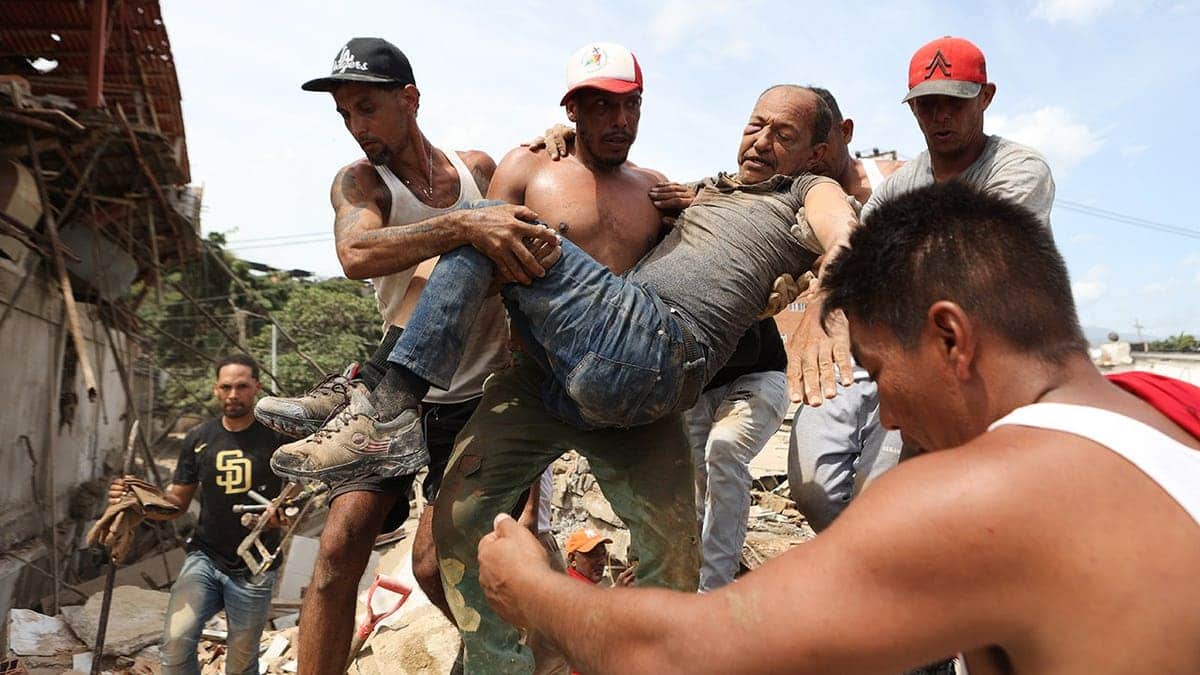 Neighbors carrying a man rescued from rubble of collapsed building in La Guaira