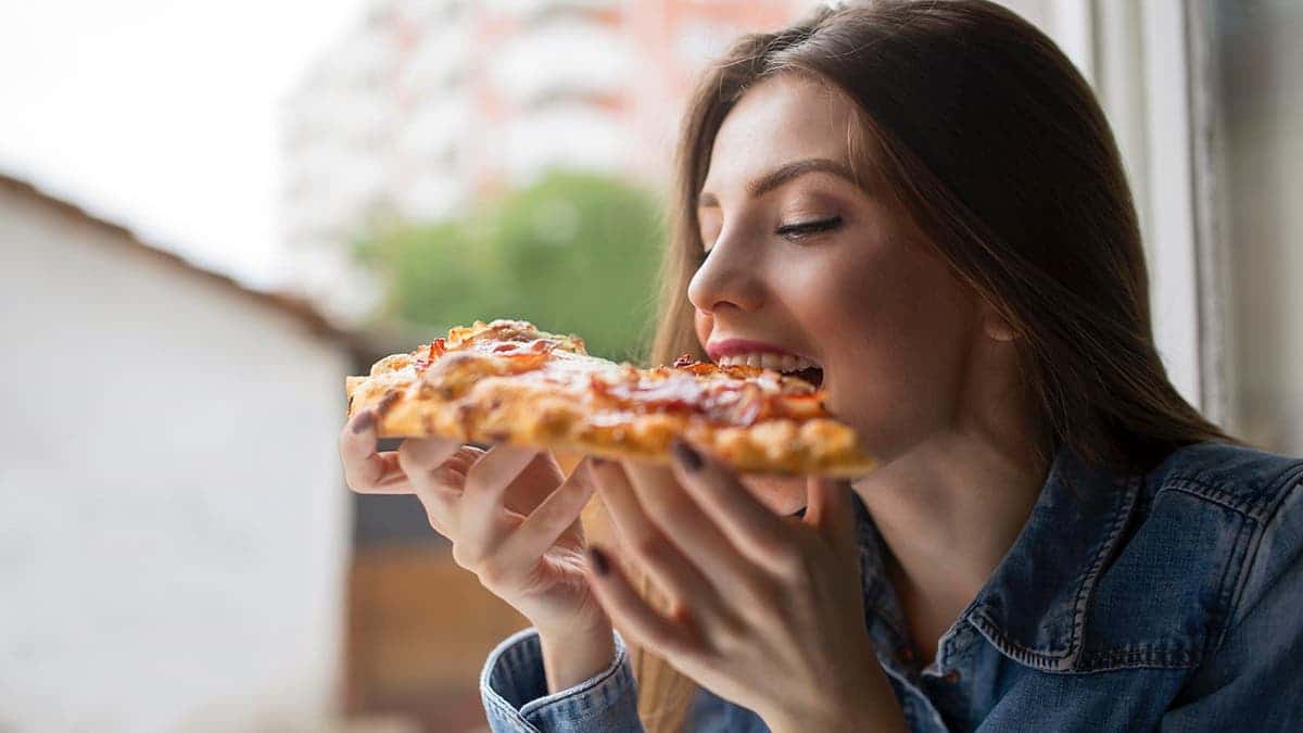 A woman bites a slice of pizza.