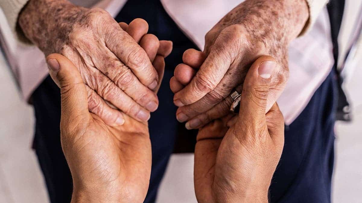 A young person holds the hands of an old person.