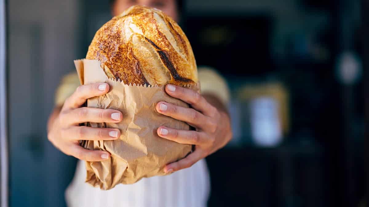 A woman holds up a loaf of sourdough bread.