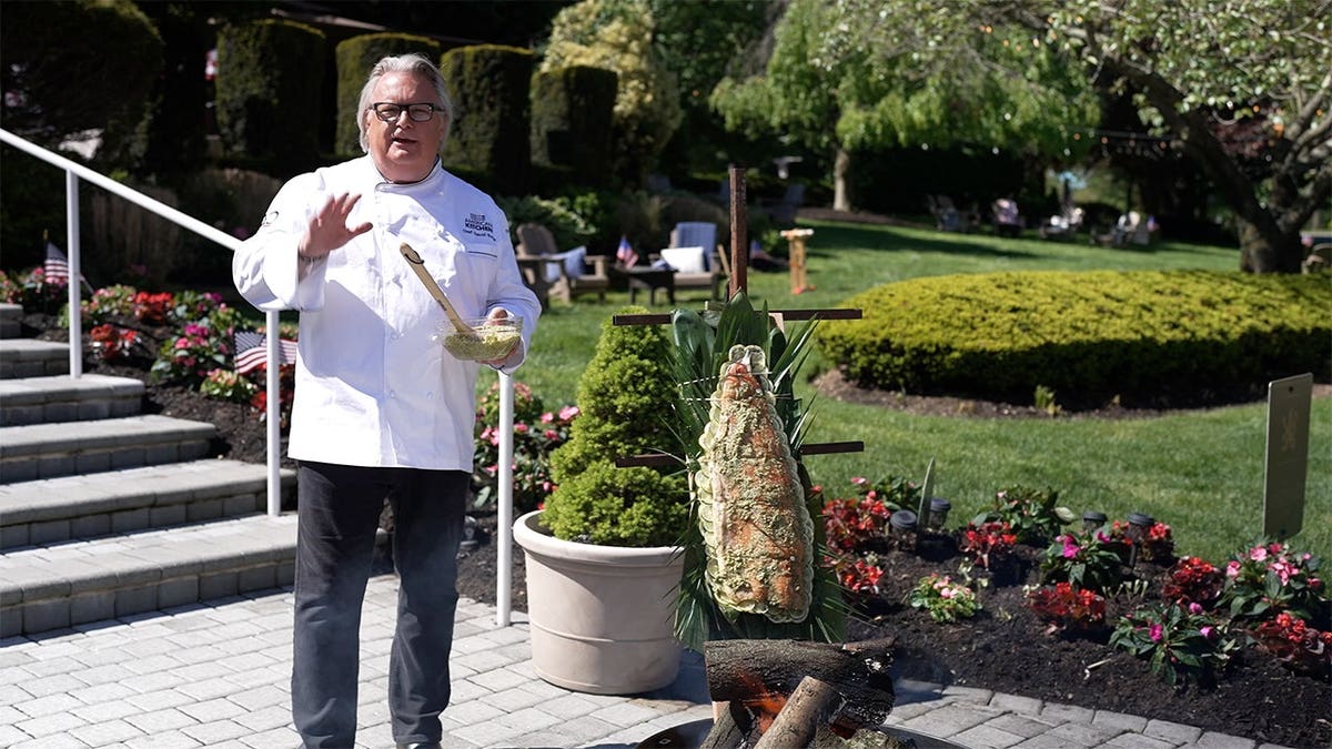 Chef David Burke holds a cedar plank salmon outdoors, showcasing the grilled seafood dish in an outdoor setting.