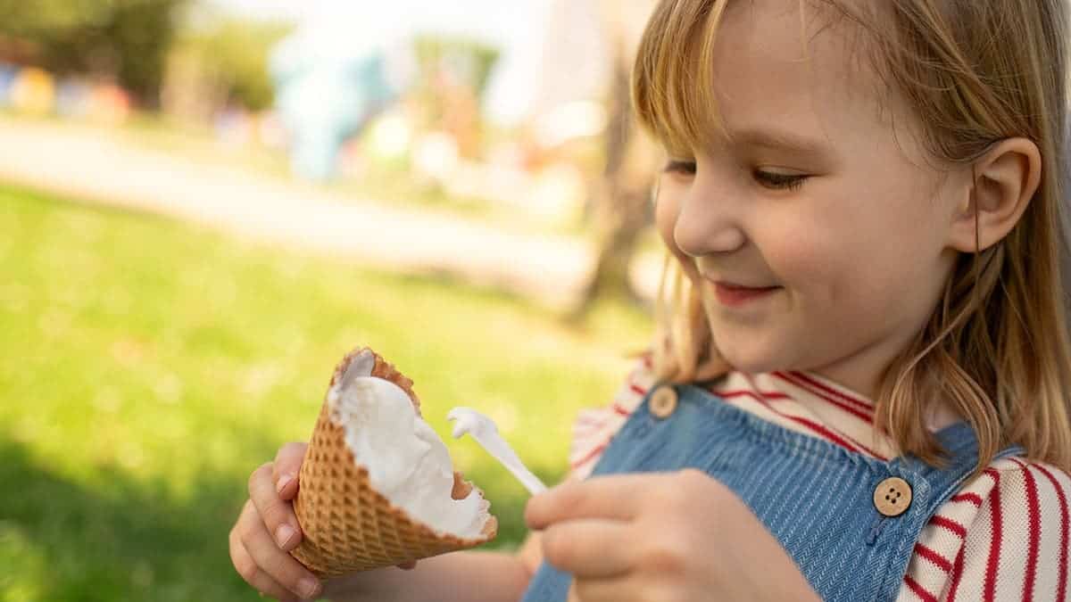A child uses a spoon to eat a dish of vanilla ice cream.