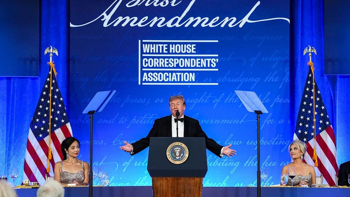 Donald Trump speaks at a podium during the White House Correspondents Dinner in a ballroom.