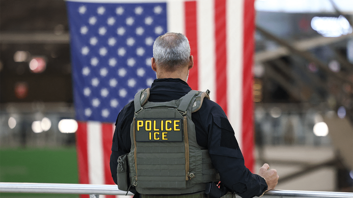 ICE agent stands before American flag as Haitian TPS enforcement operations loom.