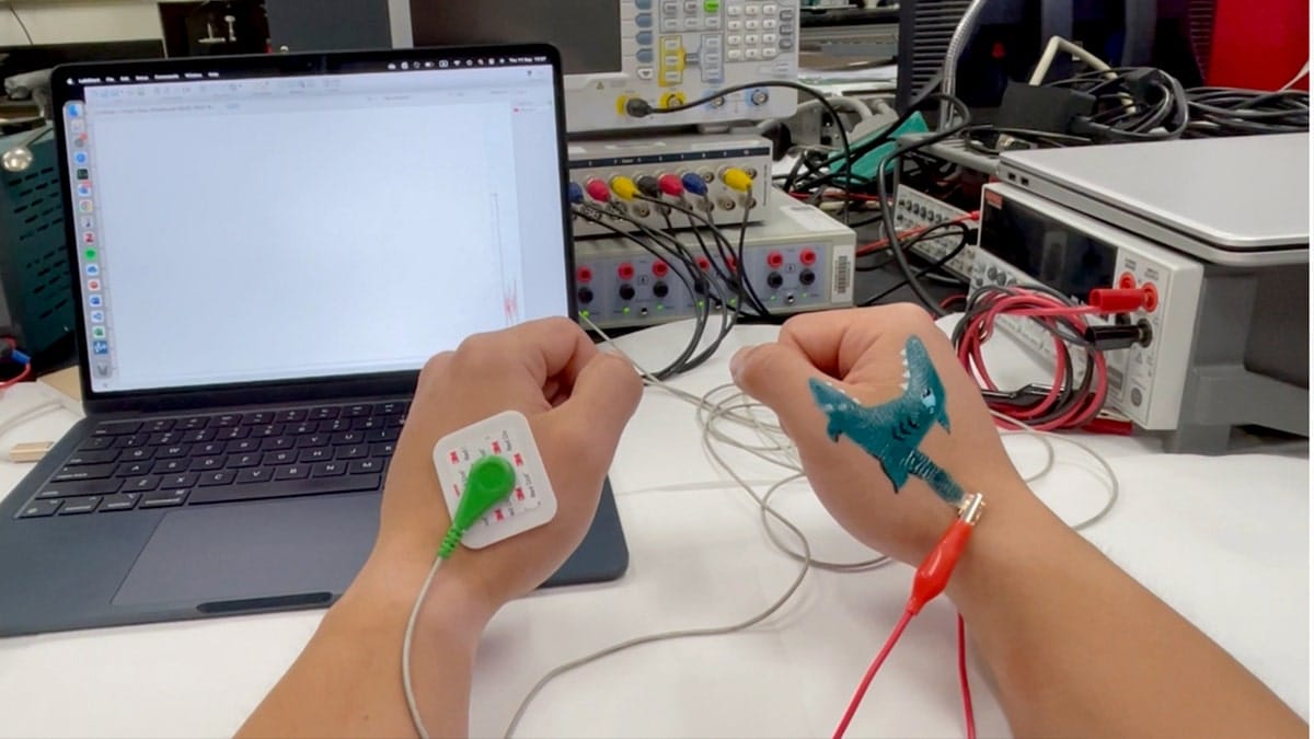 Wires are attached to two hands with painted tattoos.