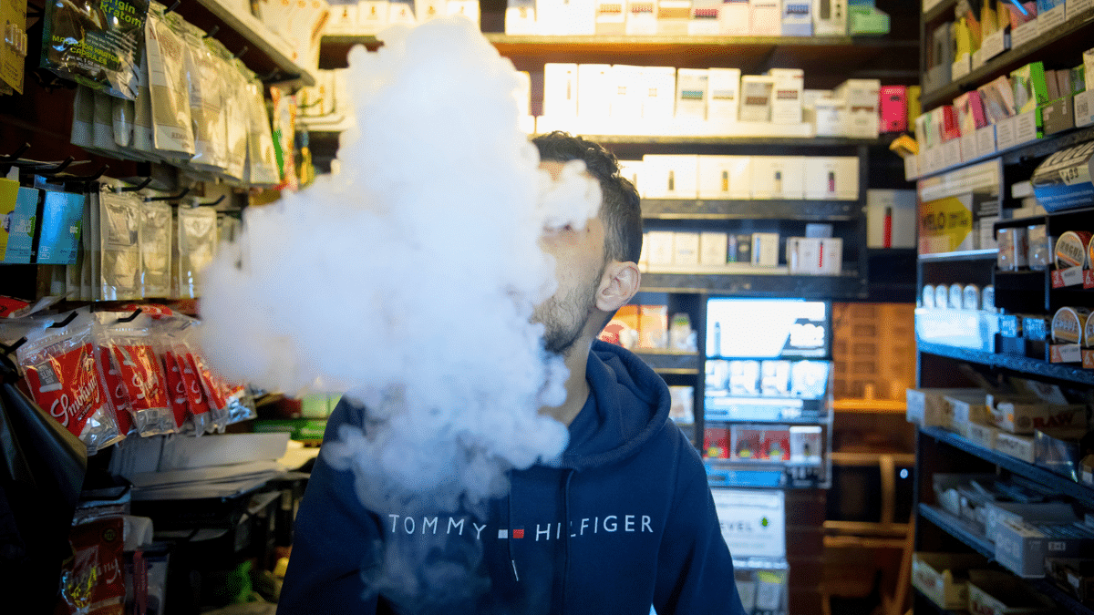 A person exhales vapor while using an electronic cigarette device at a smoke shop in New York.