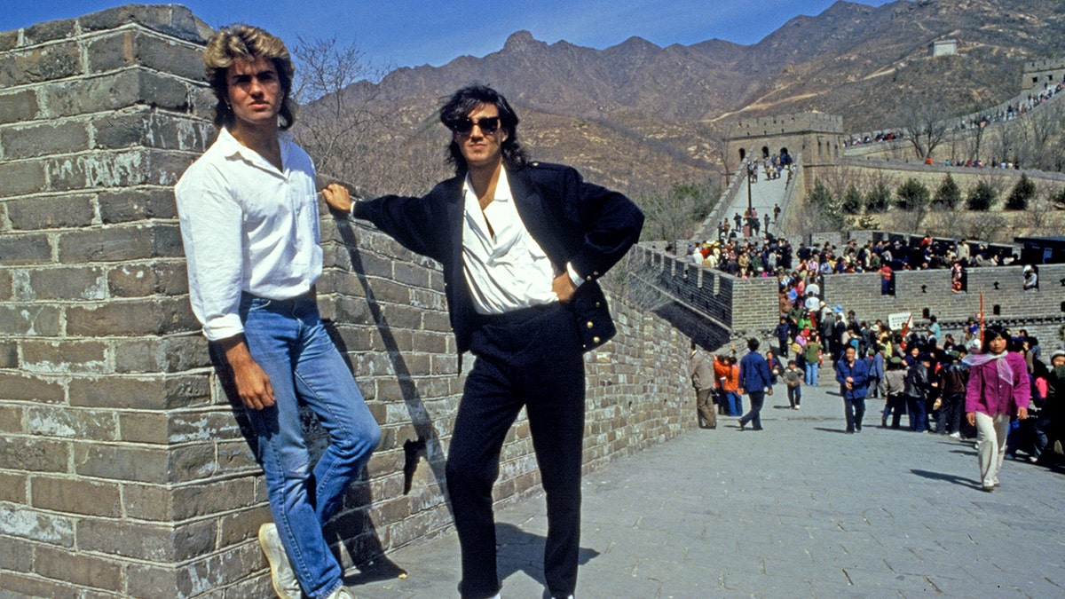 Andrew Ridgeley and George Michael pose on the Great Wall of China with visitors walking behind them.