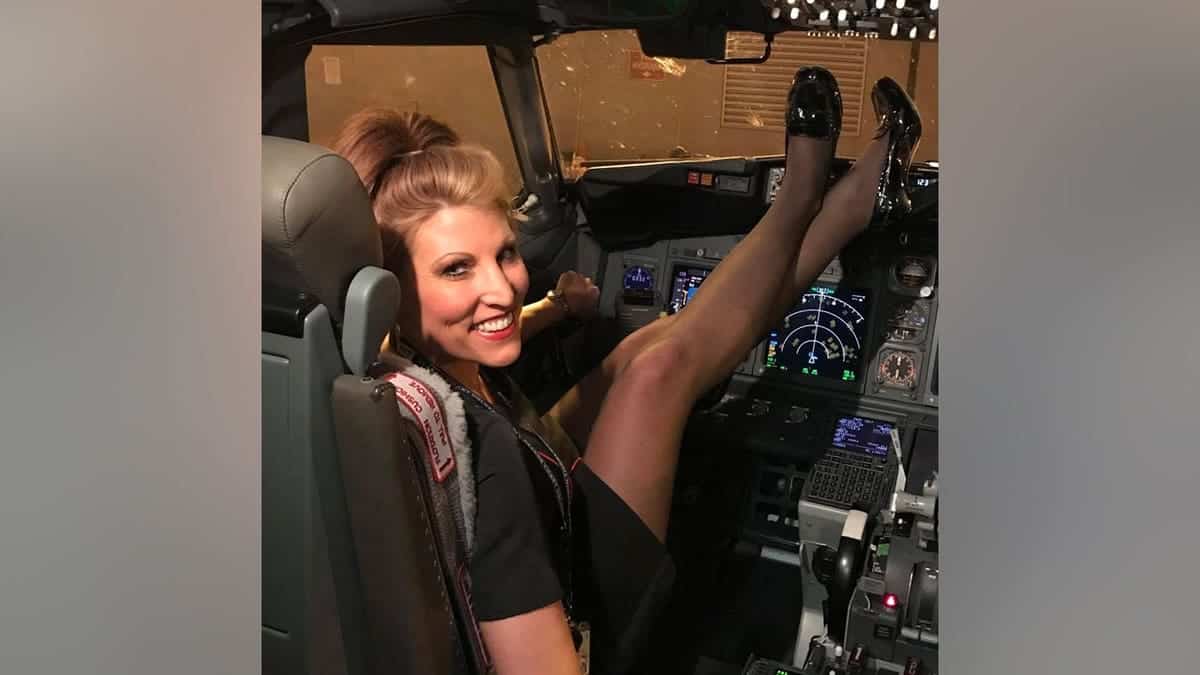 Jenny Lupton smiles while seated in an airplane cockpit, resting her feet on the flight deck console.